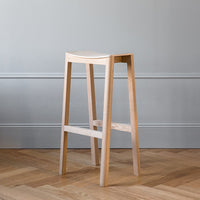 Light wood bar stool with a smooth, natural finish against a textured gray wall and herringbone wood floor.