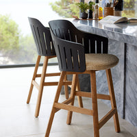 Black and natural wood bar stools with slatted backs and woven seats, set against a light marble countertop.