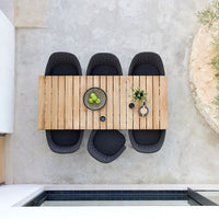 "Natural wood table with black cushioned chairs, featuring a minimalist design and a neutral concrete backdrop."