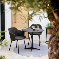 Modern gray upholstered chairs paired with a sleek black round table on a soft circular rug. Stylish outdoor dining setup.