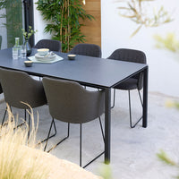 Modern black dining table with gray upholstered chairs, set against a neutral background with greenery accents.