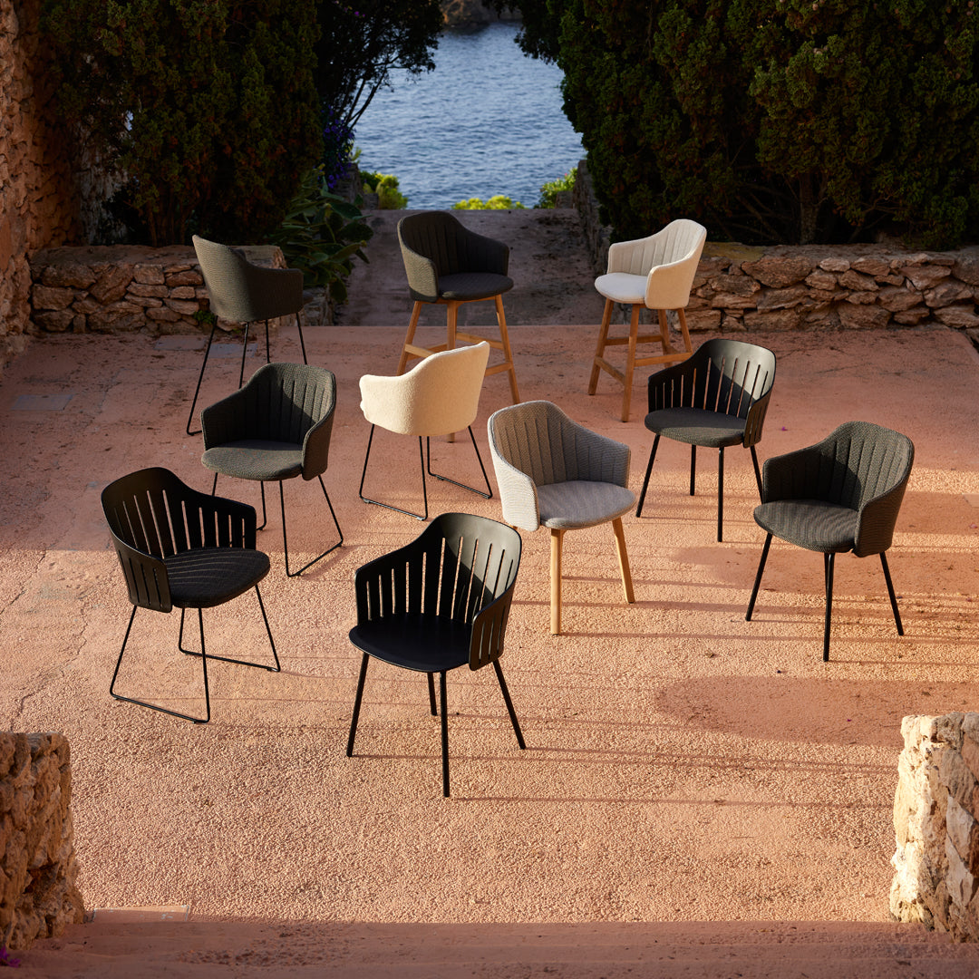 Nine stylish chairs in black, white, and gray, featuring modern designs and various leg finishes, arranged outdoors.