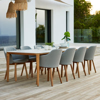 Light gray modern dining chairs with natural wood legs around a white table, set on a warm-toned wooden patio.