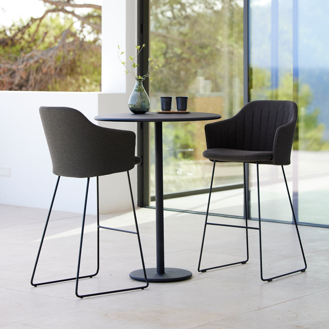 Modern black and gray bar stools with a sleek metal frame and ribbed upholstery, paired with a minimalist black table.