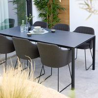 Modern black dining table with gray upholstered chairs, showcasing a minimalist design against a natural backdrop.