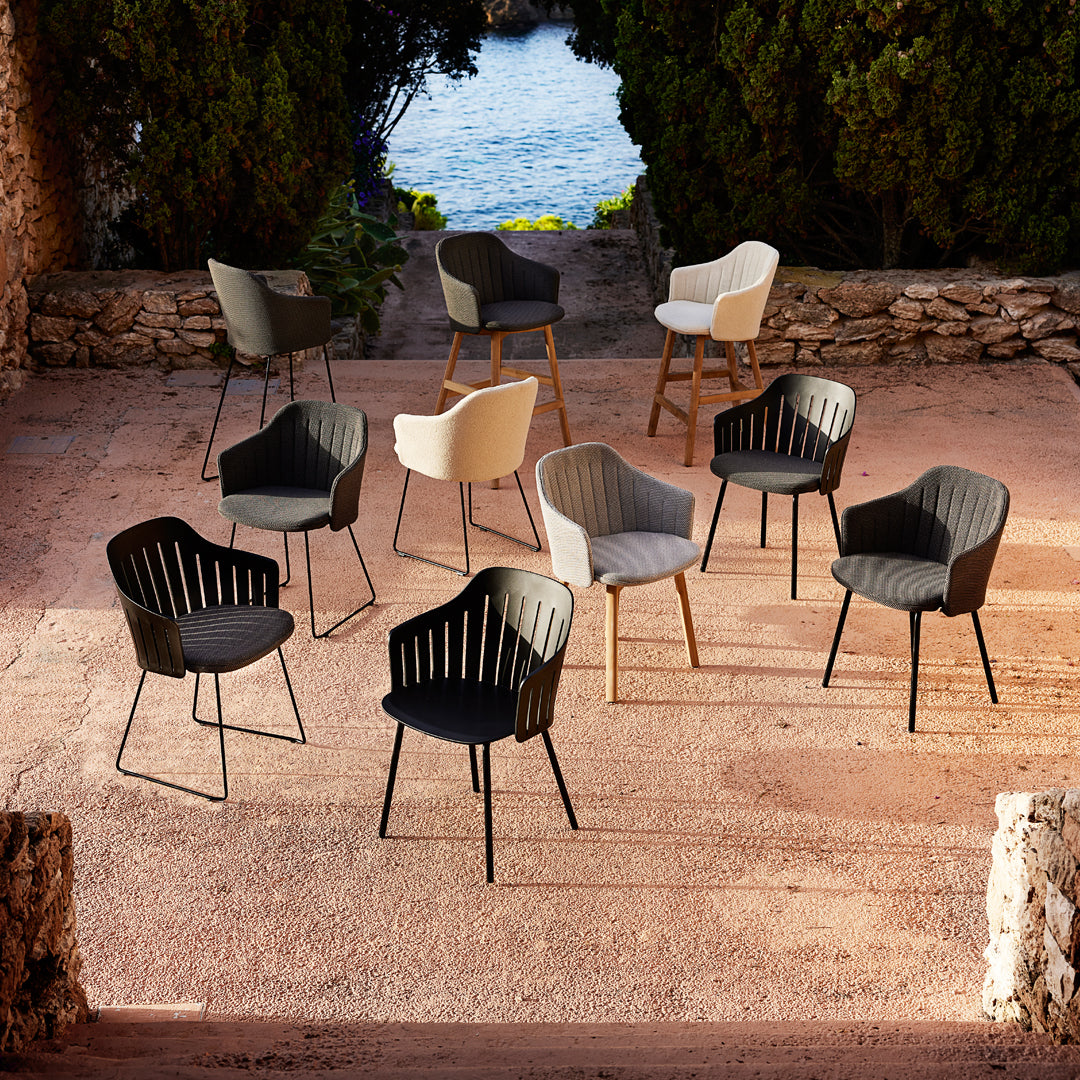 "Collection of modern chairs in black, white, and gray with textured patterns, set outdoors against a scenic backdrop."