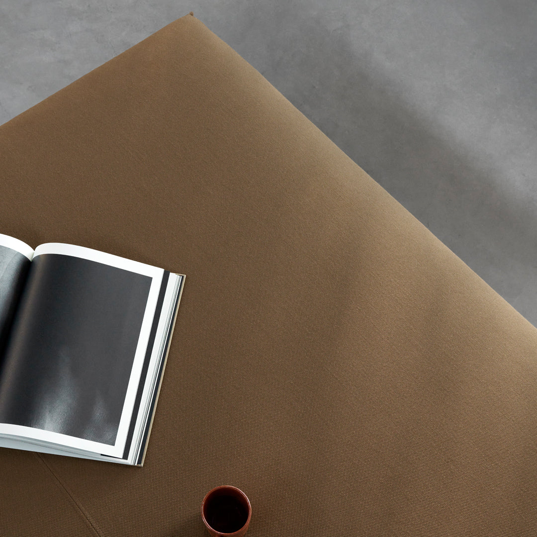 Brown textured surface with a subtle sheen, accompanied by a black and white book and a small red cup.