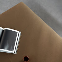 Brown textured surface with a subtle sheen, accompanied by a black and white book and a small red cup.
