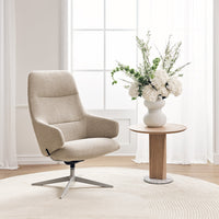 Beige upholstered chair with smooth texture, surrounded by neutral tones and natural floral arrangements.