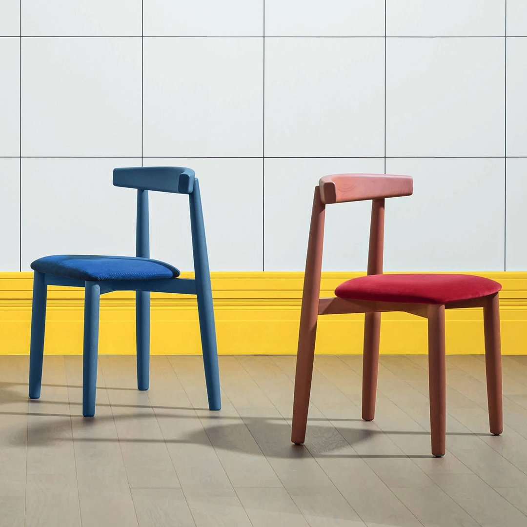 Two modern chairs in vibrant blue and red with simple, sleek designs against a bright yellow and white tiled backdrop.