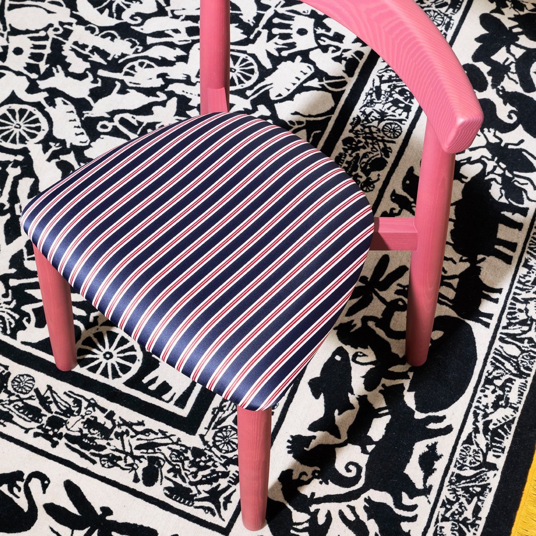 Pink chair with striped navy and red seat fabric on a contrasting black-and-white patterned rug.