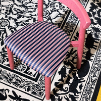 Pink chair with striped navy and red seat fabric on a contrasting black-and-white patterned rug.