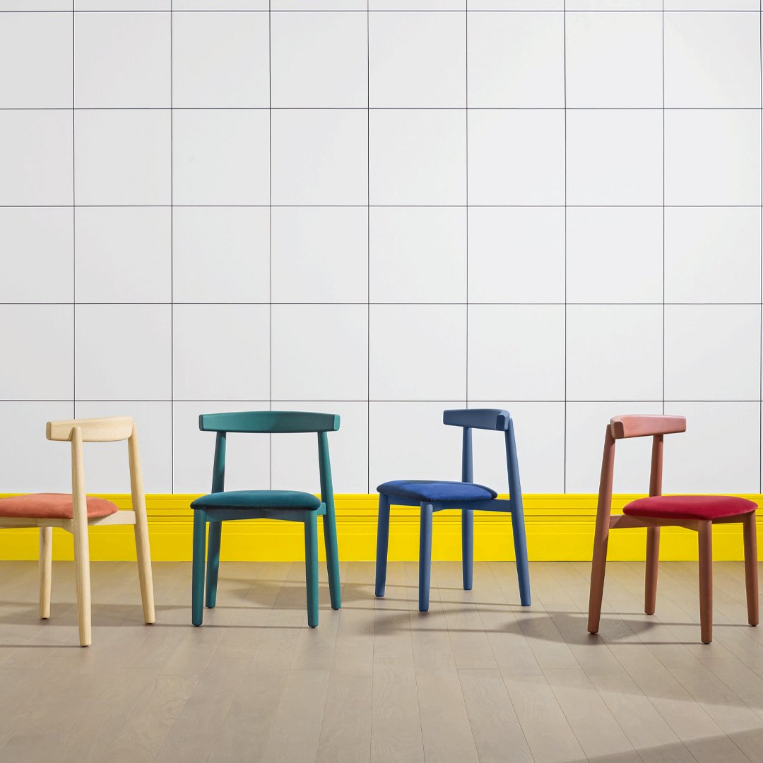 "Colorful chairs in yellow, blue, green, red, and natural wood against a white tiled background."