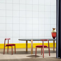 Modern dining room scene featuring a glass table with wood legs, red accent chairs, and a bright yellow wall.
