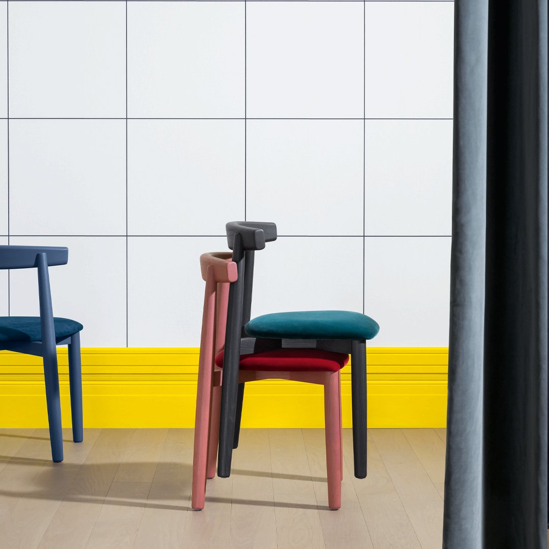 Colorful stacked chairs featuring blue, pink, black, and teal against a white tiled wall and yellow baseboard.