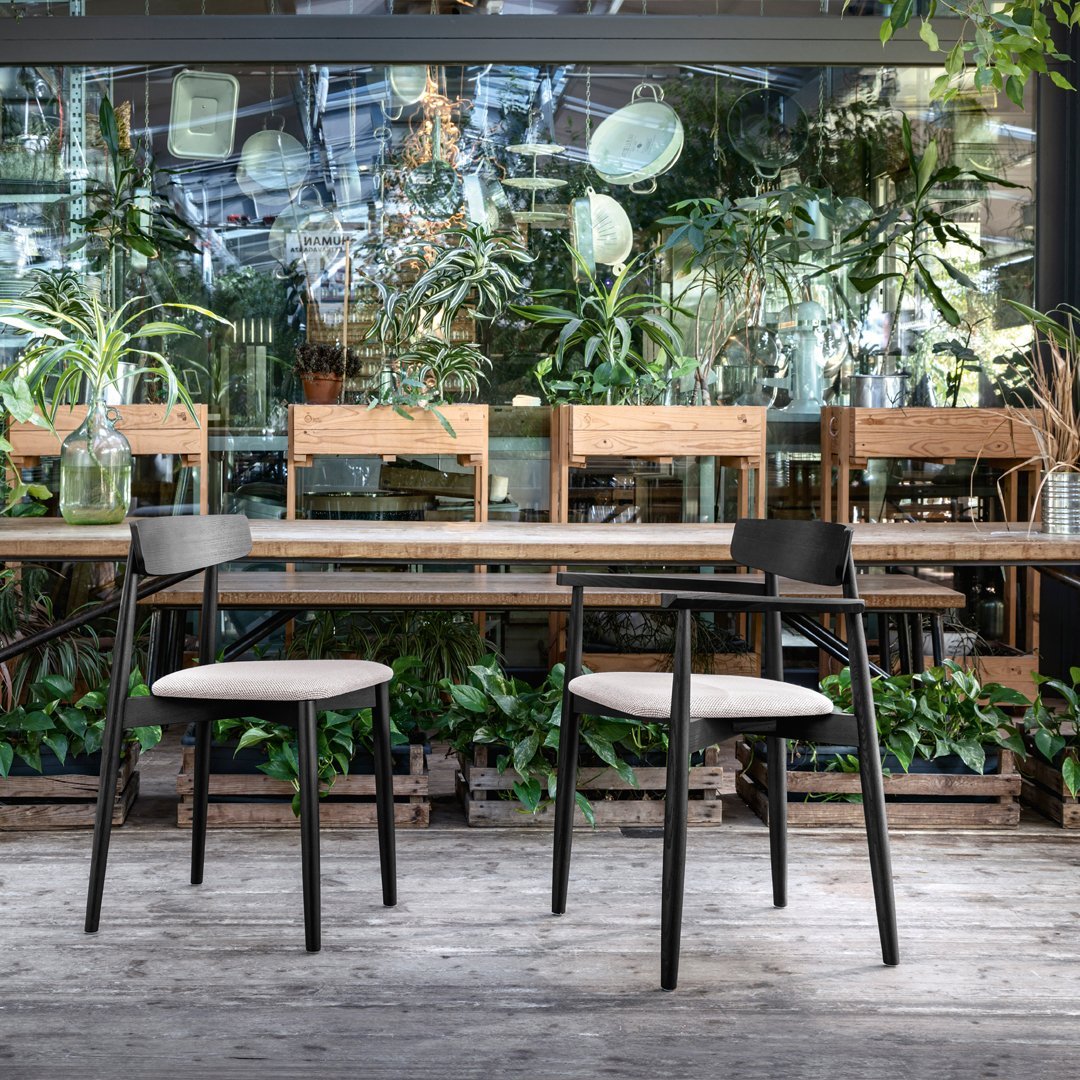 Black wooden chairs with beige cushions, set against a backdrop of greenery and wooden furniture, showcasing modern design.