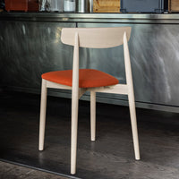 Modern wooden chair with a light wood frame and vibrant orange upholstered seat, set against a sleek metal backdrop.