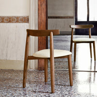 Wooden chair with a light cream seat and natural wood finish, set against a classic patterned wall.