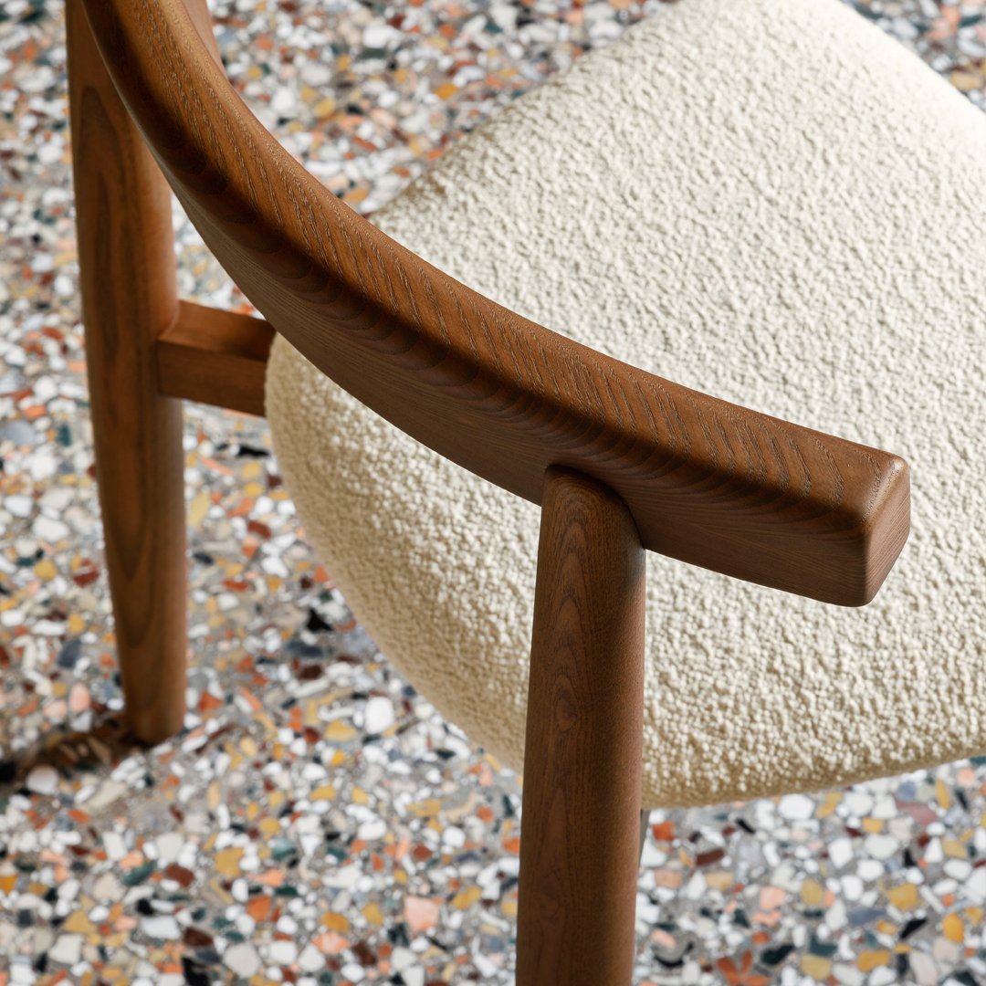 Close-up of a cream textured chair seat with warm wooden armrests, set against a colorful terrazzo floor.