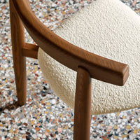 Close-up of a cream textured chair seat with warm wooden armrests, set against a colorful terrazzo floor.