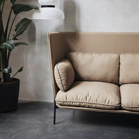 Beige upholstered sofa with plush cushions and a sleek black frame, set against a subtle gray wall.