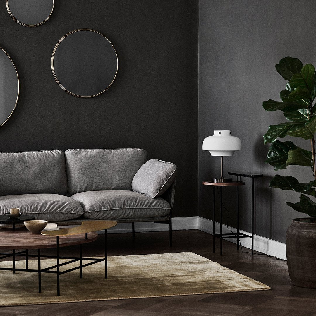 Gray sofa on a dark wall, with gold accents, black furniture, and a beige area rug. Modern and sophisticated design.
