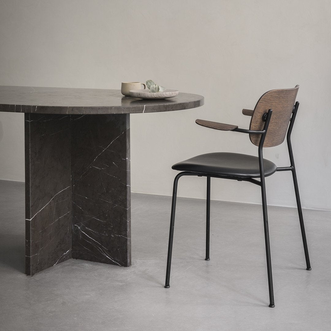 Elegant black and wood chair next to a round dark marble table against a soft gray floor. Minimalist design and neutral tones.