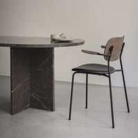 Elegant black and wood chair next to a round dark marble table against a soft gray floor. Minimalist design and neutral tones.