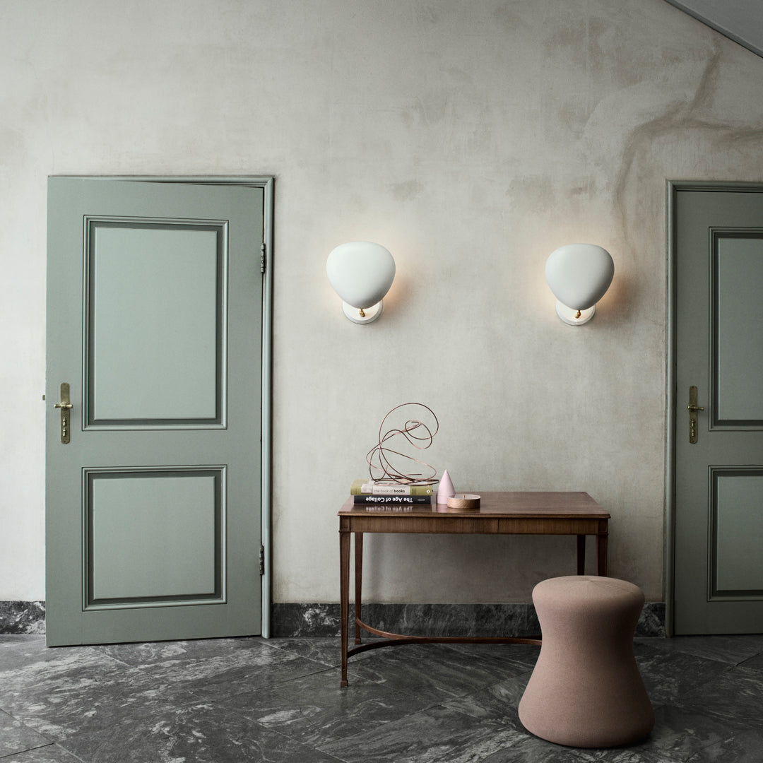Stylish mint green doors and walls with rounded white wall sconces and a soft pink stool on a textured gray floor.