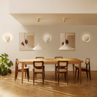 Wooden dining table with brown chairs, white pendant lights, and soft beige walls. Modern art in muted tones.