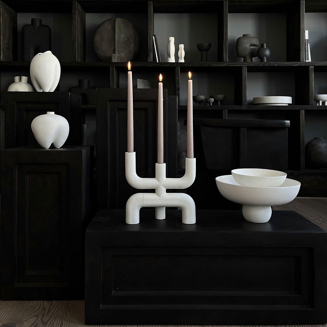 Elegant white ceramic candle holder with gray candles, set against a minimalist black backdrop and assorted decor.