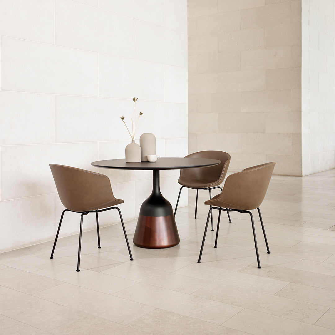 Elegant round table with a brown and black base, complemented by chic brown chairs in a minimalist space.