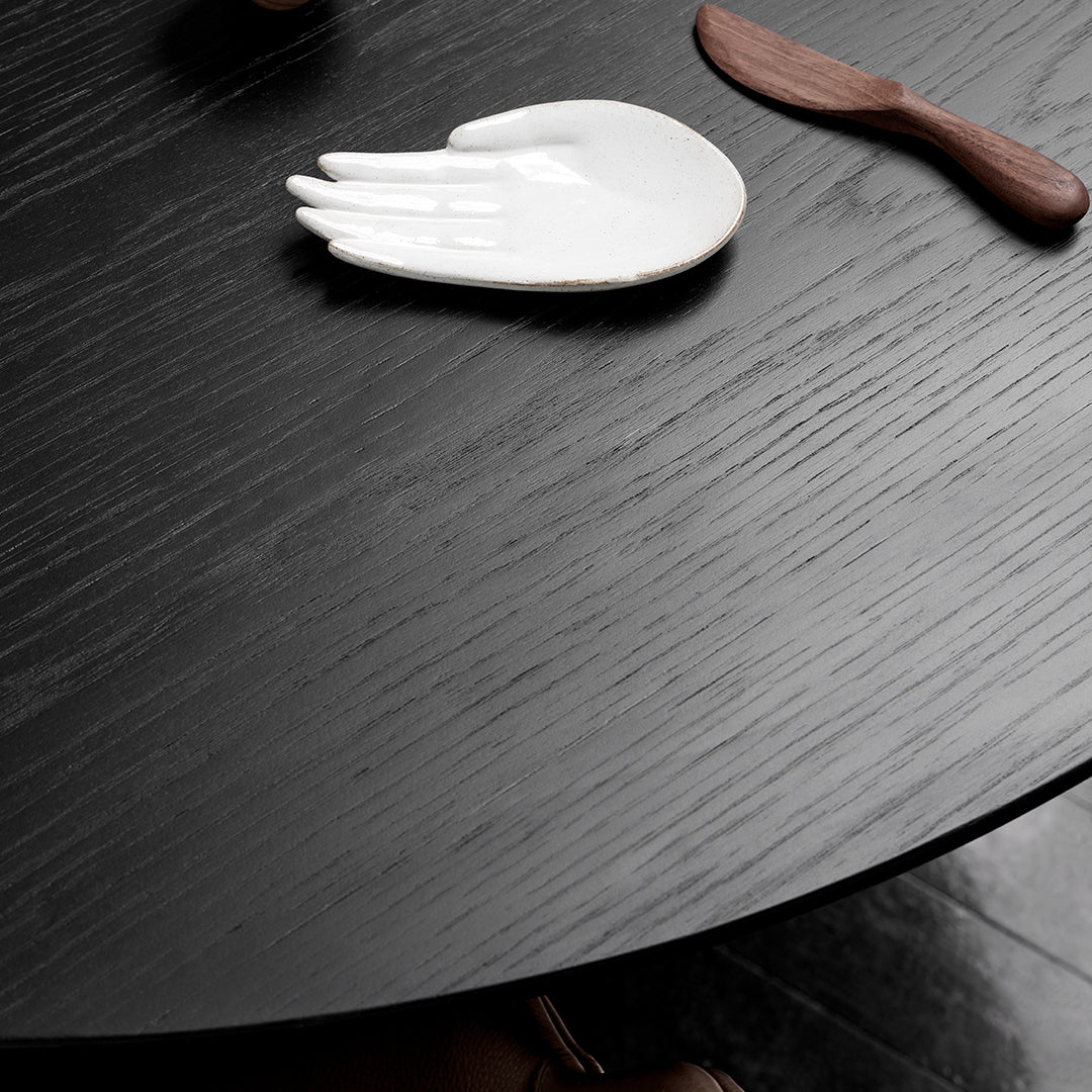 Black wood table surface with subtle grain, featuring a white hand-shaped dish and a brown wooden utensil.