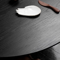 Black wood table surface with subtle grain, featuring a white hand-shaped dish and a brown wooden utensil.