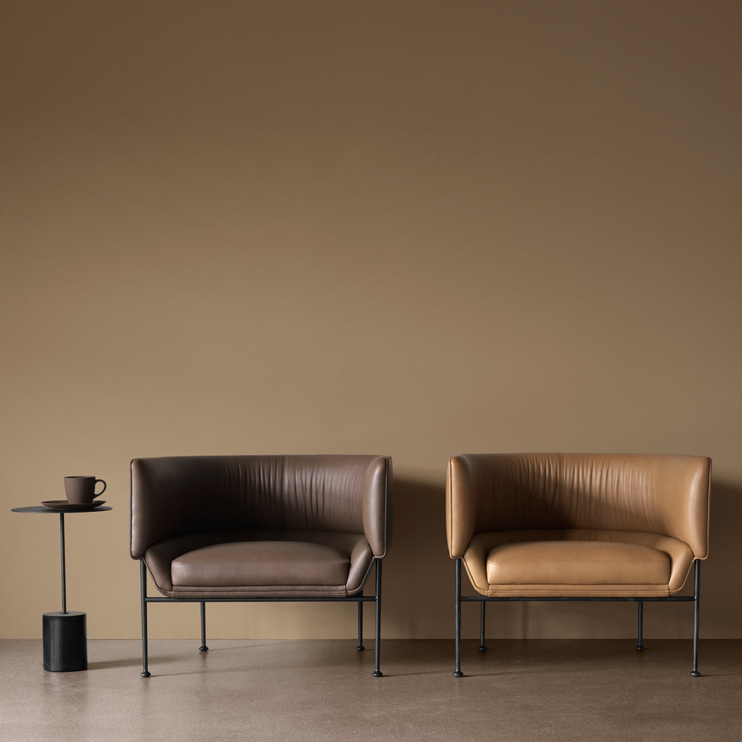 Brown and tan leather armchairs with a sleek black side table against a warm beige wall. Modern and stylish design.