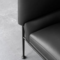 Black leather sofa with sleek, minimalistic design and subtle stitching details on a gray concrete background.
