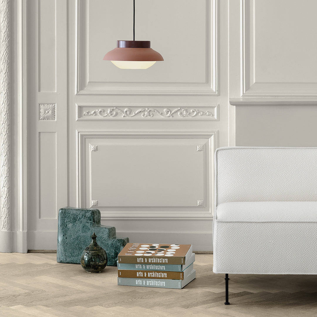 Rustic pink pendant light against a sleek white wall, complementing earthy tones of stacked books and decor.