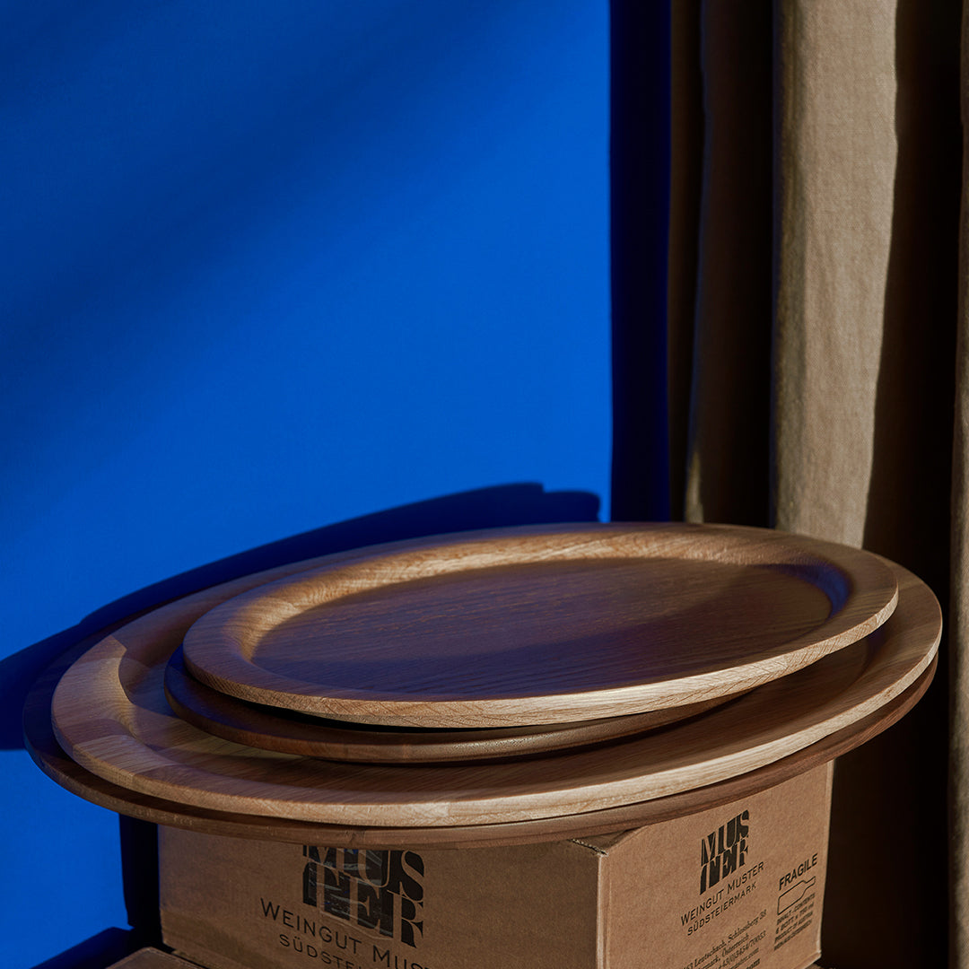 Wooden serving plates with smooth, curved edges against a vibrant blue background and neutral beige drapery.