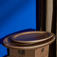 Wooden serving plates with smooth, curved edges against a vibrant blue background and neutral beige drapery.