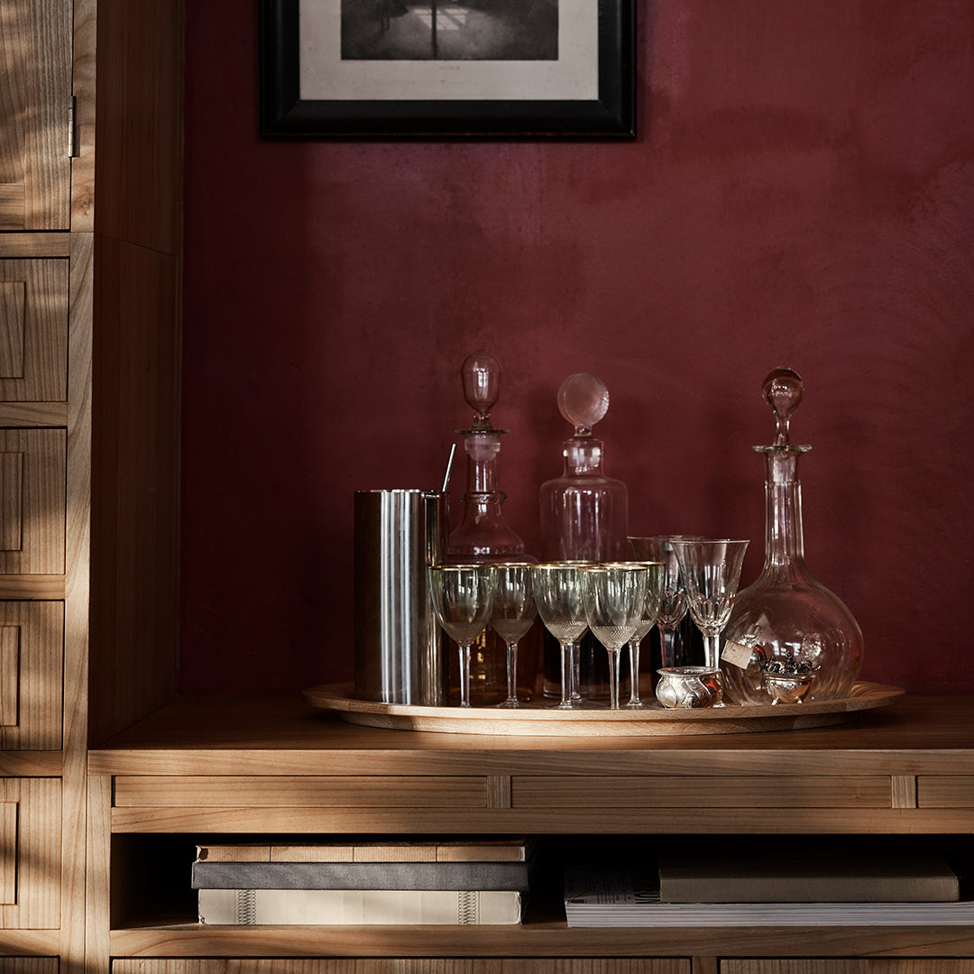 Elegant glassware displayed on a wooden tray, featuring clear, frosted, and reflective surfaces against a deep red backdrop.
