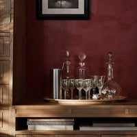 Elegant glassware displayed on a wooden tray, featuring clear, frosted, and reflective surfaces against a deep red backdrop.