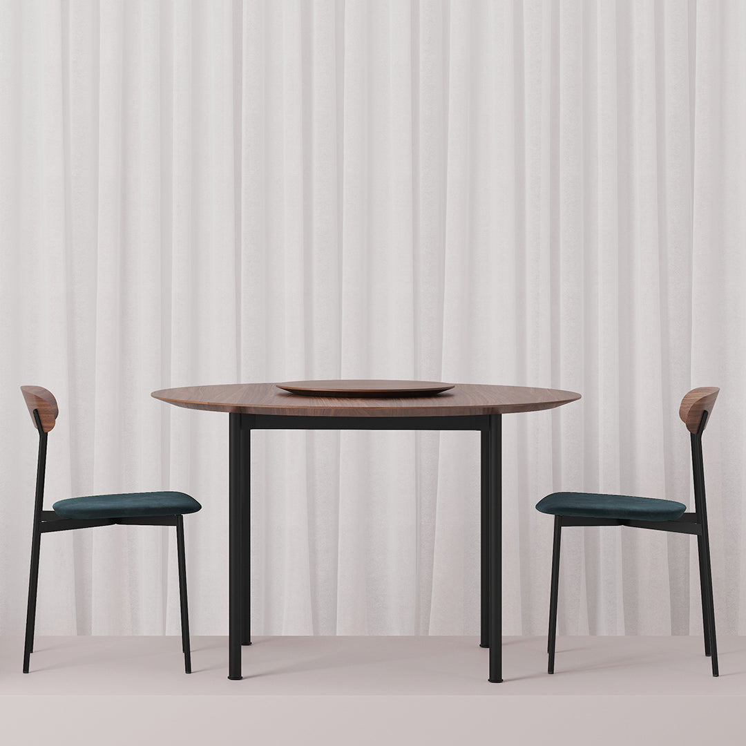 Modern round table with a dark wood top and black legs, paired with teal cushions and light wood accents on chairs.