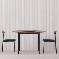 Modern round table with a dark wood top and black legs, paired with teal cushions and light wood accents on chairs.