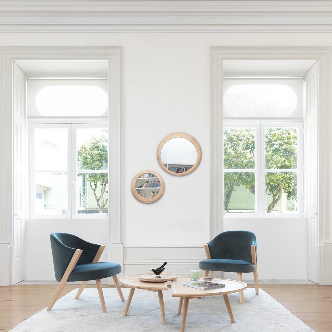 "Modern blue velvet chairs with light wood accents, set against a bright, airy room with circular mirrors and natural light."