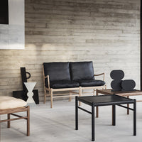 Modern black leather sofa with wooden frame, minimalistic black table, and abstract neutral decor against a concrete backdrop.