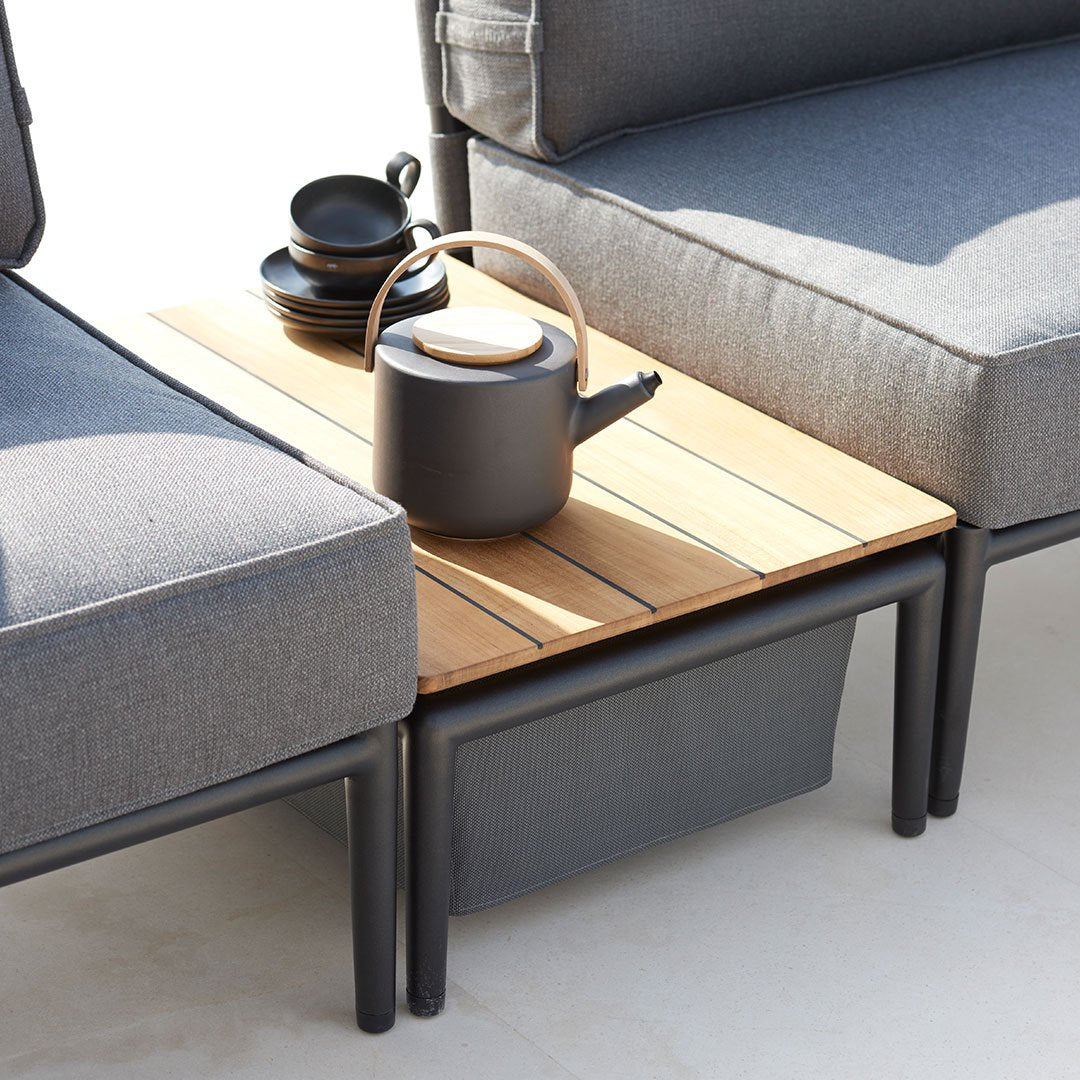 Gray fabric lounge chairs with a wooden slatted coffee table, featuring a black teapot and plates. Minimalist and modern design.
