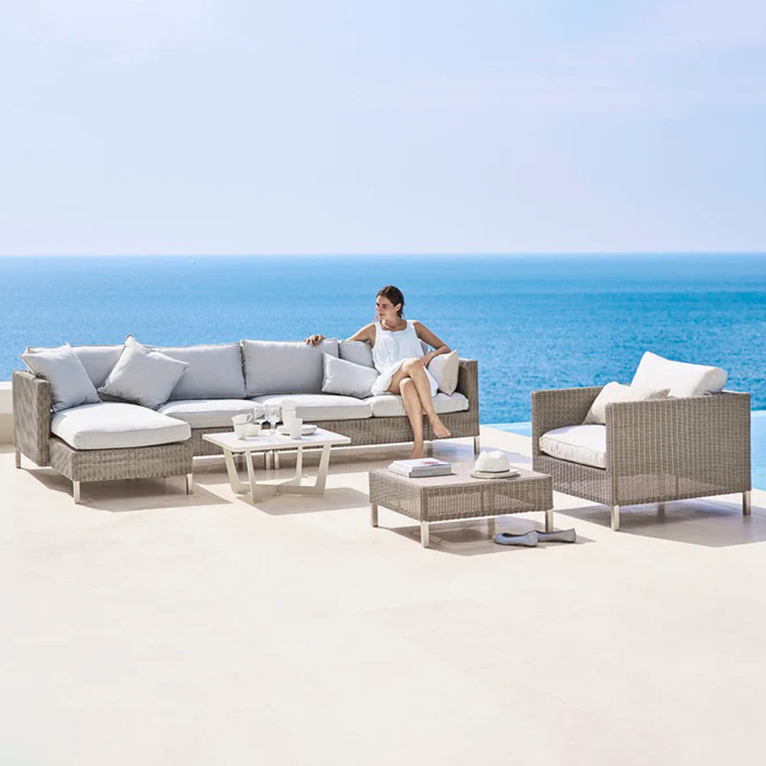 Light gray outdoor sectional sofa with white cushions, set against a tranquil blue ocean backdrop.