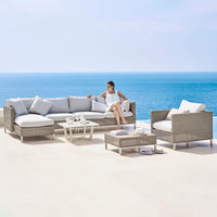 Light gray outdoor sectional sofa with white cushions, set against a tranquil blue ocean backdrop.