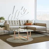 Light grey sofa with tufted pattern, circular brown and cream rug, and modern glass coffee table in bright, airy space.