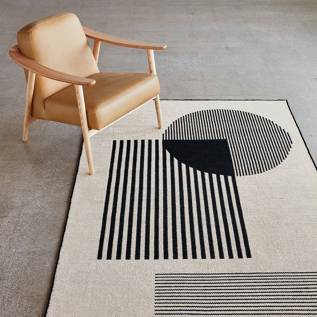 Geometric area rug featuring black and cream stripes, circles, and rectangles for a modern aesthetic.